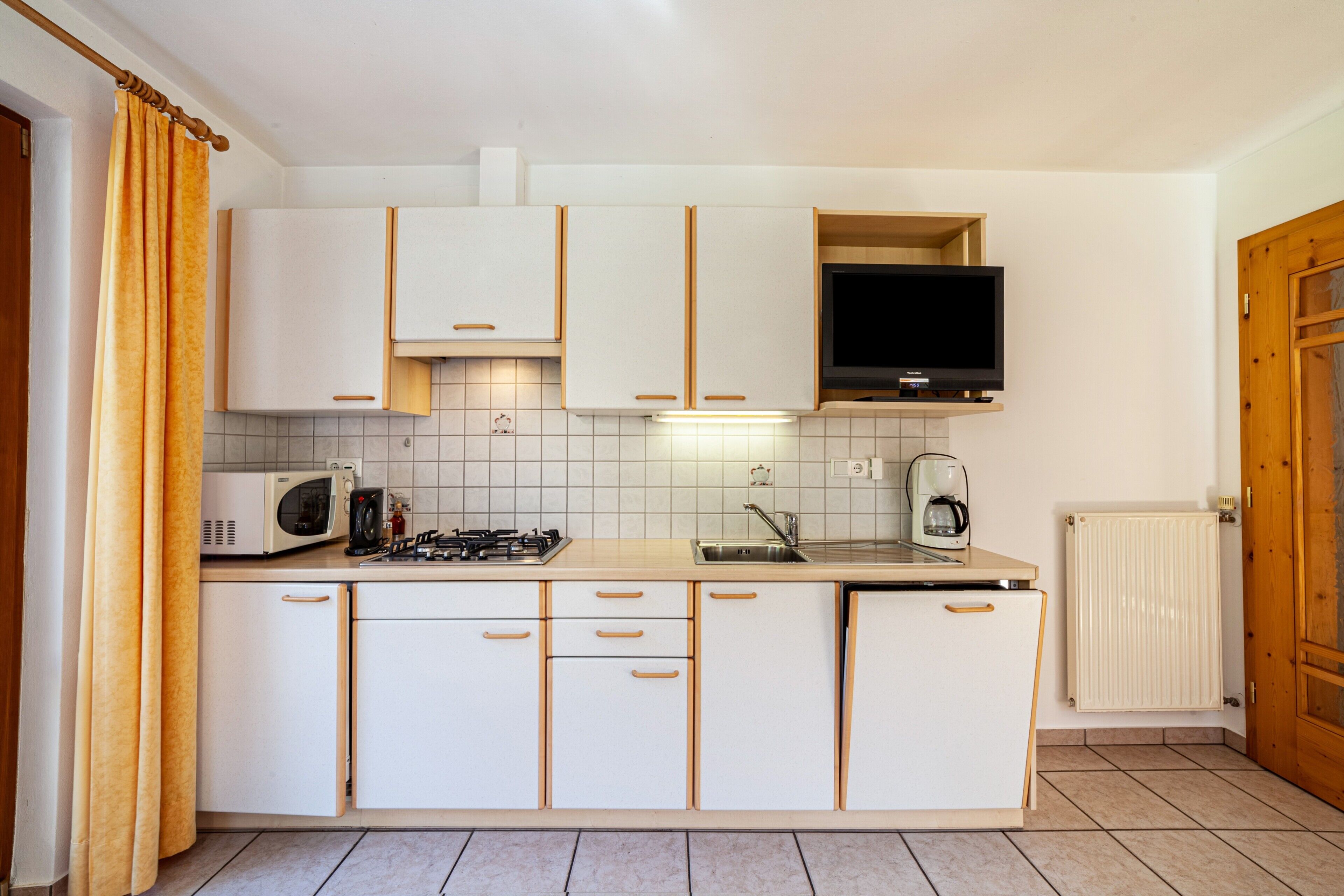 A kitchen with white cabinets, a microwave, a stove, a sink, and a television.