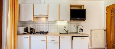 A kitchen with white cabinets, a microwave, a stove, a sink, and a television.