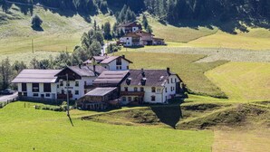 A large, multi-story building with a traditional architectural style, surrounded by lush green fields and a forested hillside. - Apartment 'Rieglhof Geiernest' with Mountain View, Garden & Wi-Fi (Graun im Vinschgau)
