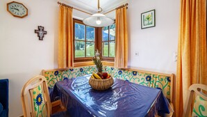 A dining area with a table covered in plastic, a fruit bowl, and a cross on the wall. - Apartment 'Rieglhof Geiernest' with Mountain View, Garden & Wi-Fi (Graun im Vinschgau)