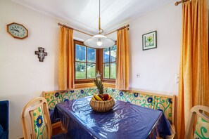 Un comedor con una mesa cubierta con plástico, un frutero y una cruz en la pared.