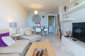 A modern living room with a sofa, coffee table, TV, and dining area.