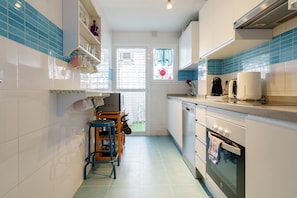 A kitchen with white cabinets, a blue tiled backsplash, a window with a view, a coffee maker, and a dishwasher.
