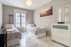 A bedroom with two beds, a dresser, a window, and a painting.