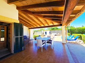 An outdoor patio with a wooden ceiling, a dining table with chairs, and a pool area with lounge chairs.