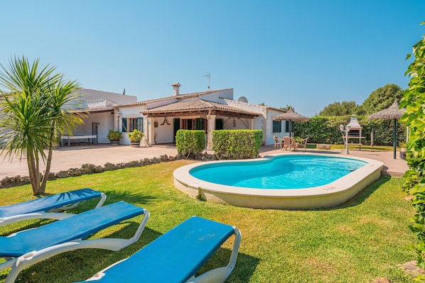 A poolside area with lounge chairs, a swimming pool, and a house with a tiled roof.