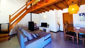 A living room with a wooden staircase, a sofa, a TV, and a dining area with chairs and a table. - Finca Villa Tranquila en Pollensa with Mountain View, Pool, Garden & Wi-Fi (pollensa)