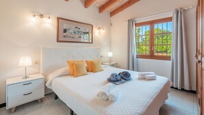 A bedroom with a bed, two bedside tables, a nightstand, a window with curtains, and a painting on the wall. - Finca Villa Tranquila en Pollensa with Mountain View, Pool, Garden & Wi-Fi (pollensa)
