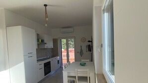A modern kitchen with white cabinets, a dining table with chairs, and a large window. - STILL HOUSE (San Nicola Arcella)