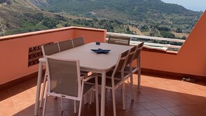 A terrace with a table and chairs, a view of green hills, and a clear sky. - STILL HOUSE (San Nicola Arcella)