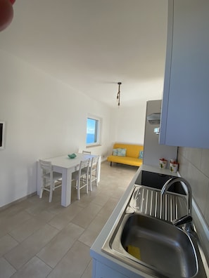 A compact kitchen with a dining area, a window, and a yellow sofa.