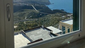 A room with a large window overlooking a coastal landscape, including a bridge and distant hills. - STILL HOUSE (San Nicola Arcella)
