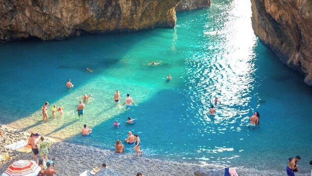 A natural rock formation with a clear blue pool and a beach area with people and umbrellas. - STILL HOUSE (San Nicola Arcella)