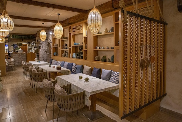 A restaurant with wooden tables and benches, hanging wicker lamps, and shelves with decorative items.