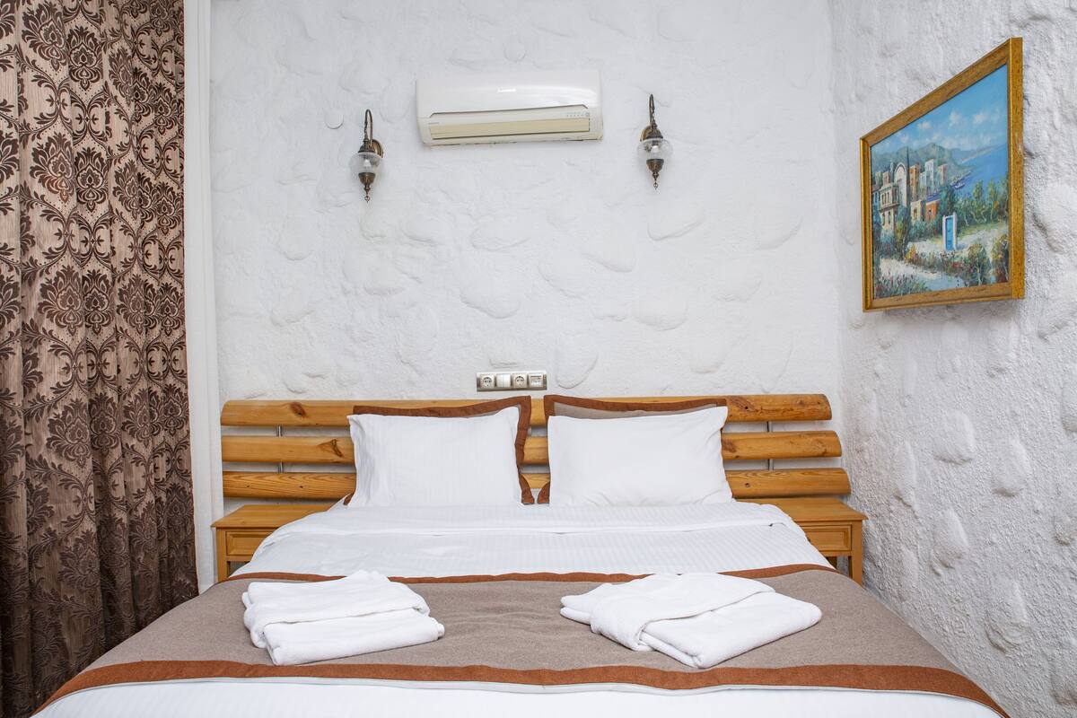 A neatly made bed with white linens, a wooden headboard, and a painting on the wall.