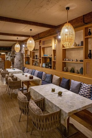 A restaurant with long communal tables, cushioned benches, and hanging wicker lamps. - Casa Galini Hotel (Ayvacik)