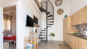 A compact living space with a spiral staircase, a kitchen with wooden cabinets, a flat-screen TV, and a small plant. - Holiday Home 'Gioberta 1' with Garden, A/C & Wi-Fi (Menfi)