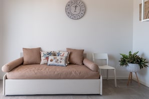 Un canapé beige agrémenté de coussins décoratifs, une chaise blanche, une horloge murale et une plante en pot.
