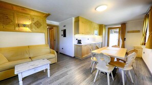 A compact living space with a sofa, dining table, chairs, and a kitchenette.