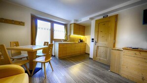 A compact kitchen with wooden cabinets, a dining table with chairs, and a window with curtains. - Flat Mont dala Nef - Baita Cusini with Mountain View, Spa Area & Wi-Fi (Livigno)