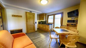 Une cuisine compacte avec des meubles en bois, une table à manger avec des chaises, un canapé et un téléviseur fixé au mur.