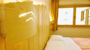 Ein Zimmer mit einem Bett, einem hölzernen Kopfteil, einem Fenster mit Vorhängen und Blick auf die Straße.