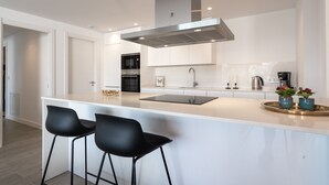 A modern kitchen with a central island, two bar stools, stainless steel appliances, and a sleek design.