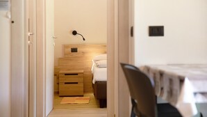 A narrow hallway leading to a bedroom with a bed, a bedside table, and a wall-mounted lamp.