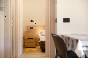 Un couloir étroit mène à une chambre à coucher qui contient un lit, une table de chevet et une lampe fixée au mur.