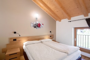 Een slaapkamer met een houten hoofdeinde, een nachtkastje met lades, een wandlamp en een raam met uitzicht.