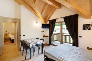 Une chambre à coucher avec un lit, une table et des chaises, une télévision et un balcon avec des rideaux.