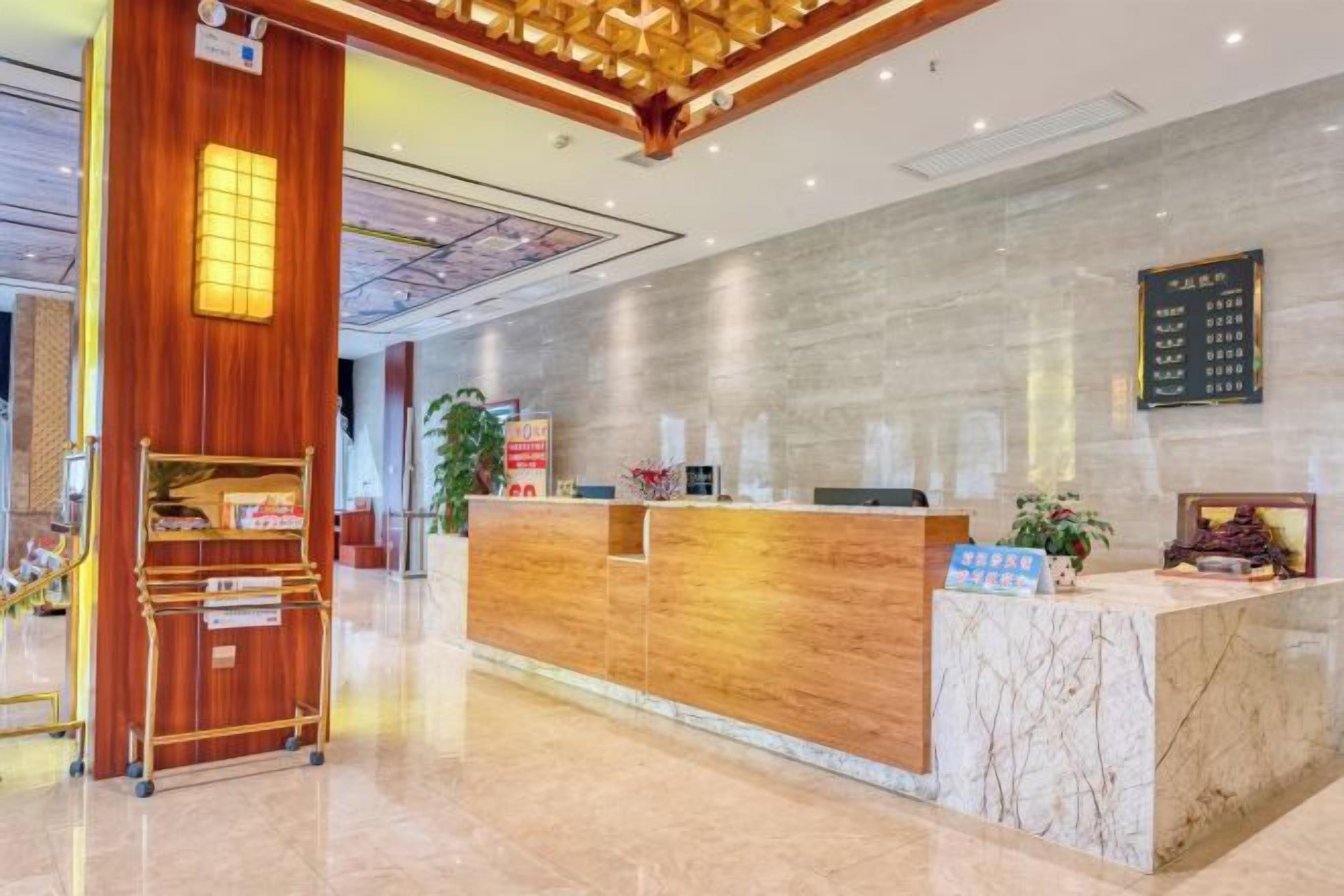 A hotel reception area with a wooden reception desk, a marble counter, and a digital directory sign.