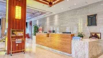A hotel reception area with a wooden reception desk, a marble counter, and a digital directory sign.