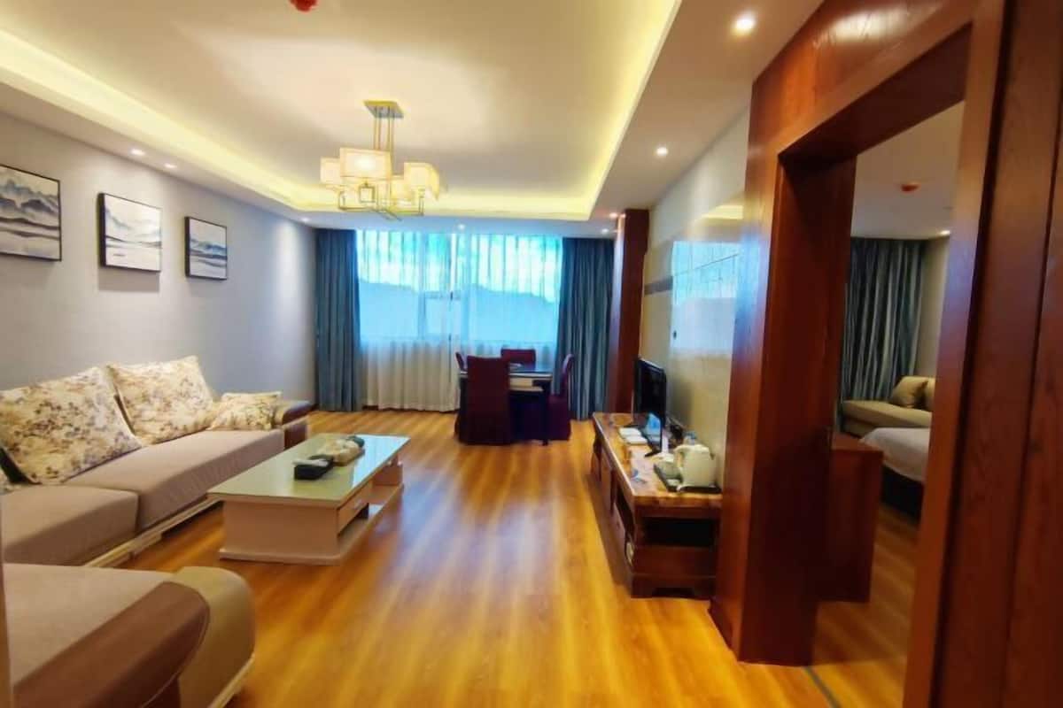 Ein modernes Wohnzimmer mit einer Couch, einem Couchtisch und einem Fernseher. Ein Holzboden und ein großes Fenster mit Vorhängen sind ebenfalls vorhanden.