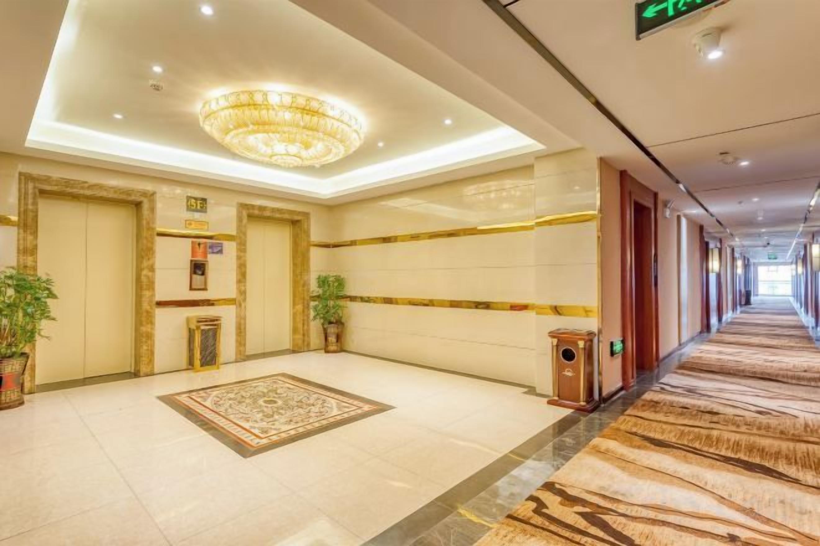 A hotel lobby with a chandelier, a patterned carpet, and a long corridor.