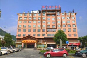 A multi-story hotel with a central entrance, parking lot, and a sign indicating a restaurant.