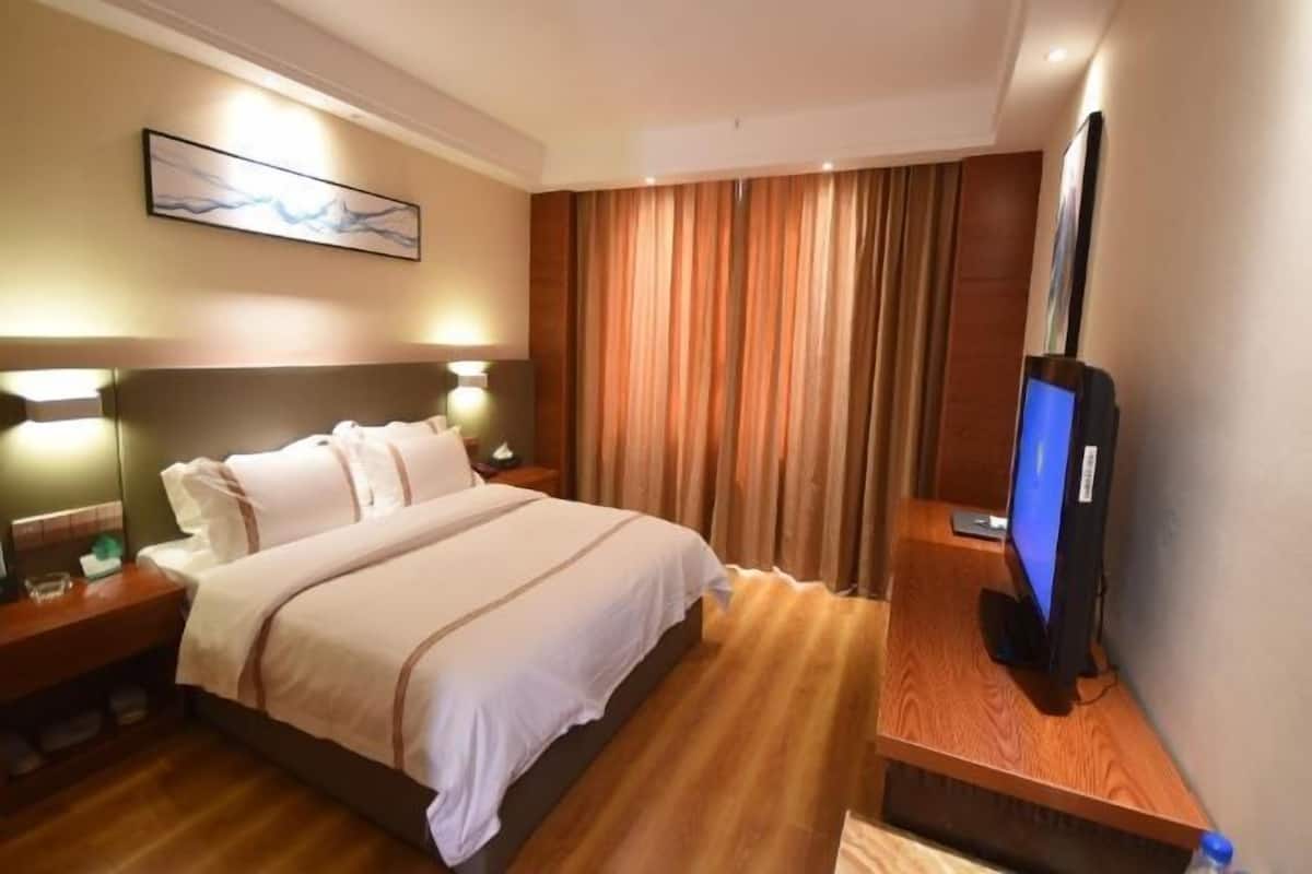 Ein Hotelzimmer mit Bett, Nachttischen, Fernseher und Vorhang.