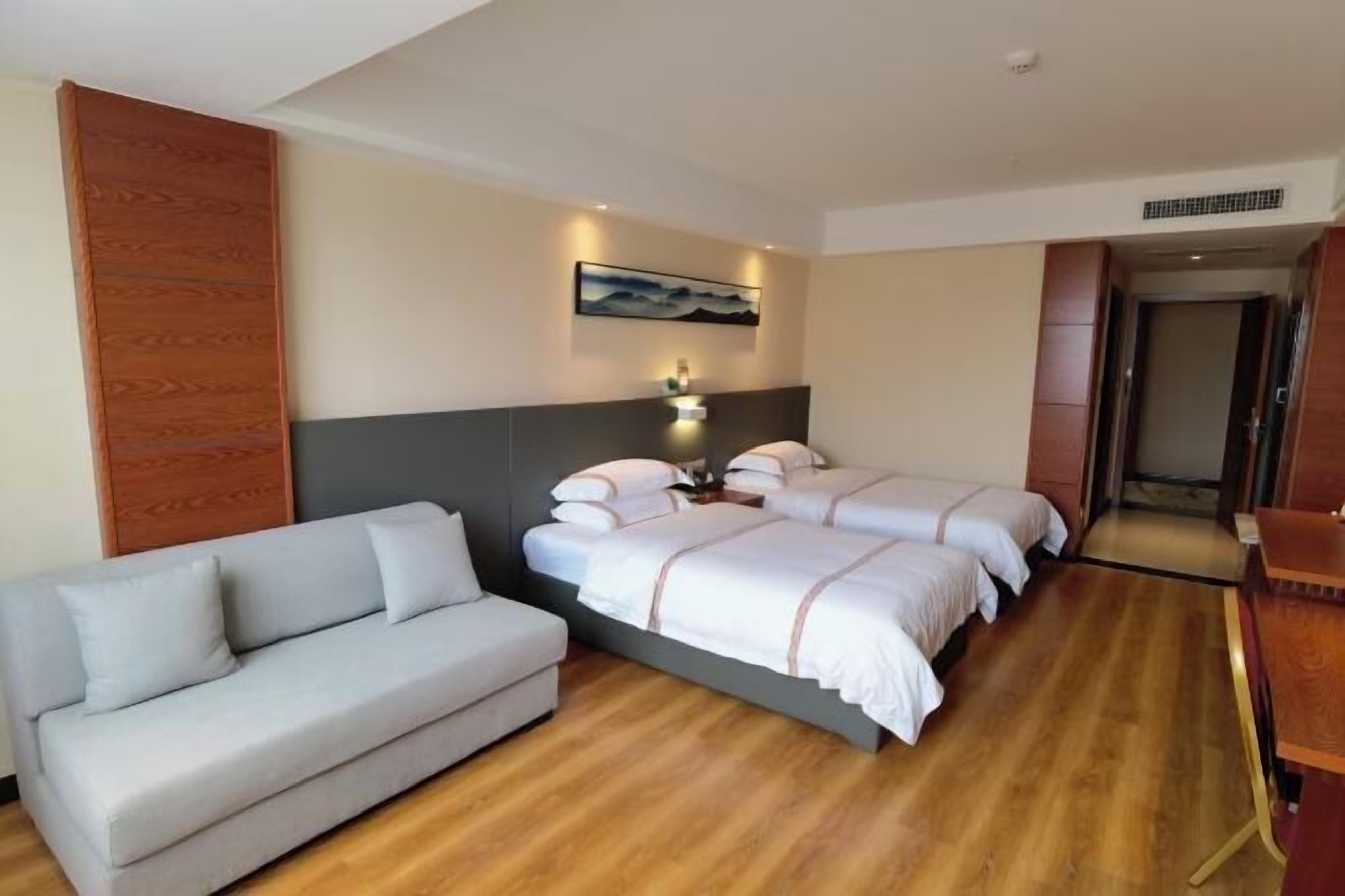 Une chambre d’hôtel avec deux lits, un canapé et un panneau en bois sur le mur de gauche.