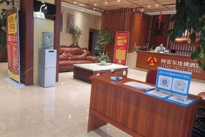 A hotel reception area with a wooden reception desk, a sofa, a coffee table, and a refrigerator.