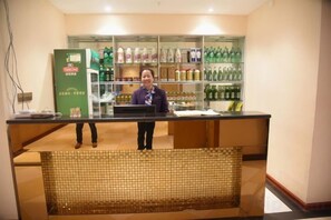 Een receptiebalie met een persoon erachter en planken vol gekoelde drankjes.