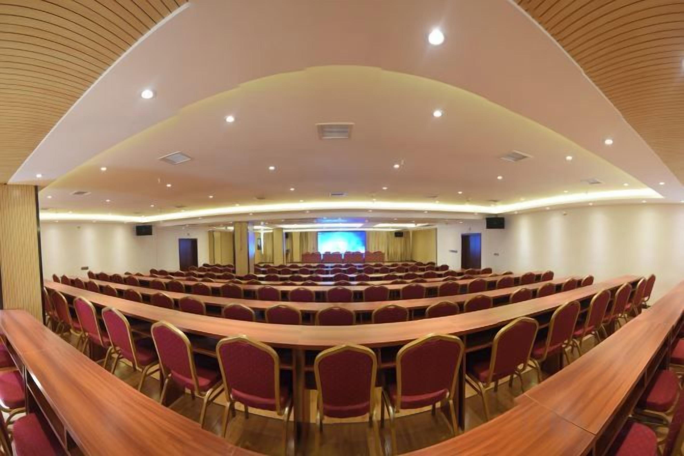 A conference room with a curved layout, multiple rows of tables and chairs, and a large screen at the front.