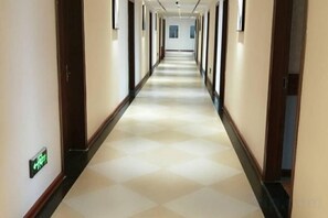 A long, narrow hallway with a checkered floor pattern, doors on both sides, and a green exit sign on the left wall. - Afuer Chain Hotel （Tianzhu Bus Station Jinfeng Park） (Tianzhu)