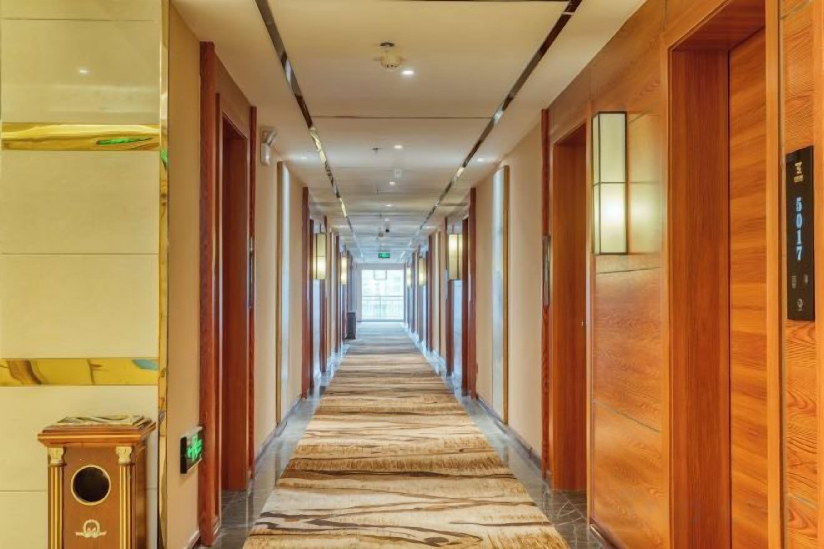 A hotel corridor with wooden doors, a patterned carpet, and a light fixture on the wall.