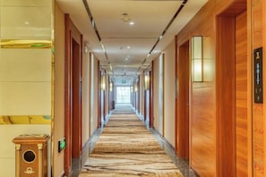 Un pasillo de hotel con puertas de madera, alfombra estampada y un aplique en la pared.