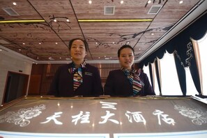 Two individuals standing behind a counter with Chinese characters, in a room with wooden ceiling and large windows.