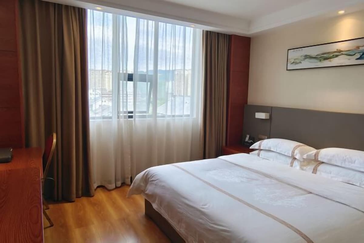 Hotellihuone, jossa on sänky, verhot, taulu ja näkymä ikkunasta.