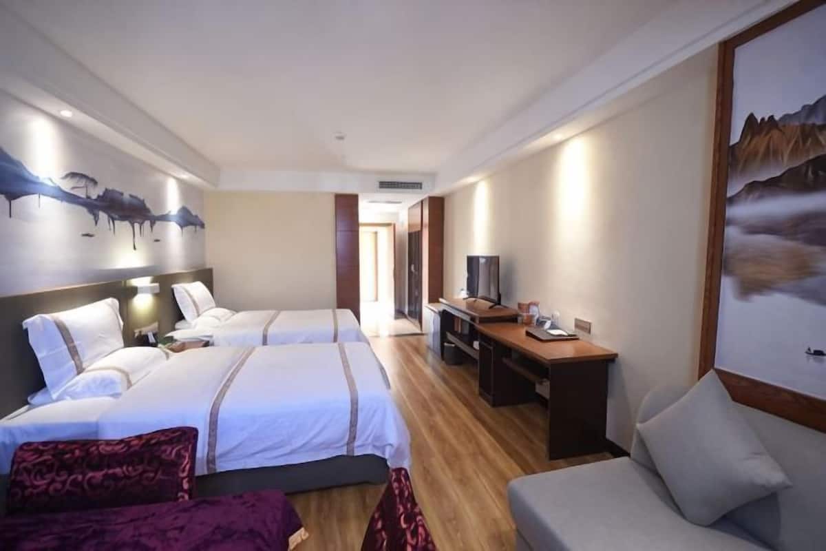 Ein Hotelzimmer mit zwei Betten, einem Schreibtisch, einem Fernseher und einem Gemälde an der Wand.
