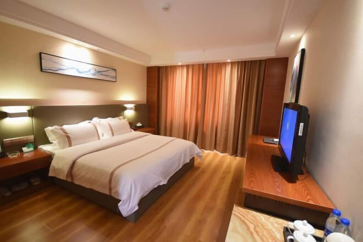 Ein Hotelzimmer mit einem großen Bett, Nachttischlampen, einem Flachbildfernseher und einem Holztisch mit einer Flasche und Gläsern.