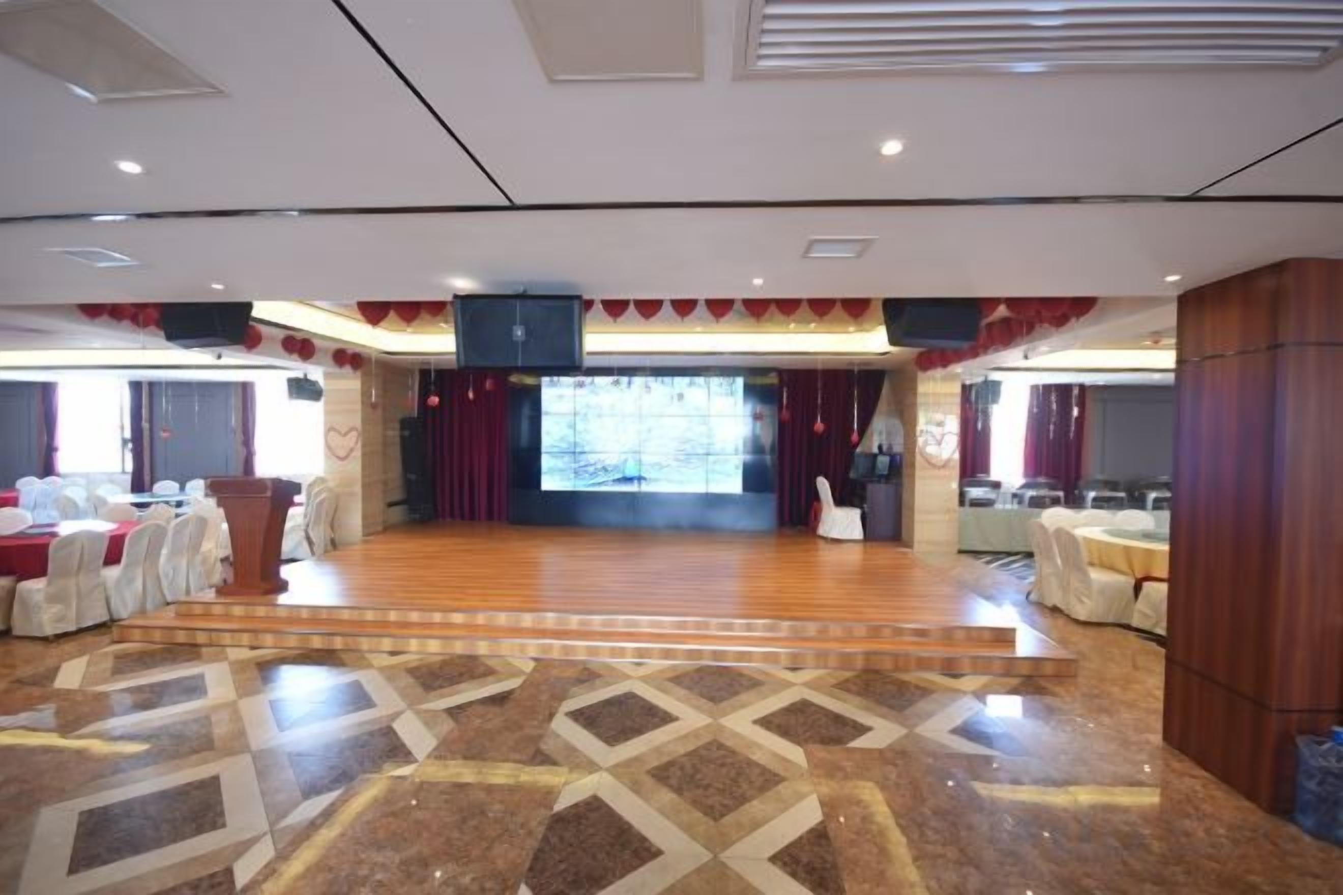 A spacious hall with a stage, seating arrangements, and a patterned floor.