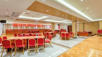 A conference room with multiple tables and chairs, a wooden floor, and a ceiling with recessed lighting.